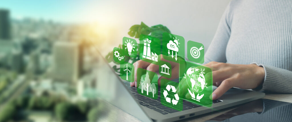 Persona con las manos en la computadora. Elementos relacionados a las responsabilidad social empresarial salen del teclado. Del lado izquiero se observa una ciudad con edificios corporativos.